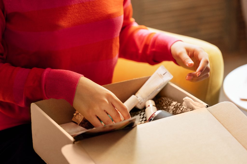 Person unboxing a CPG subscription box with beauty and skincare products inside.