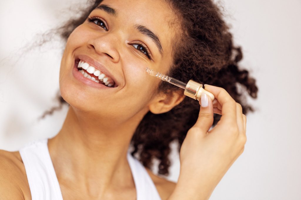 Smiling woman applying facial serum with a dropper as part of a skincare routine.