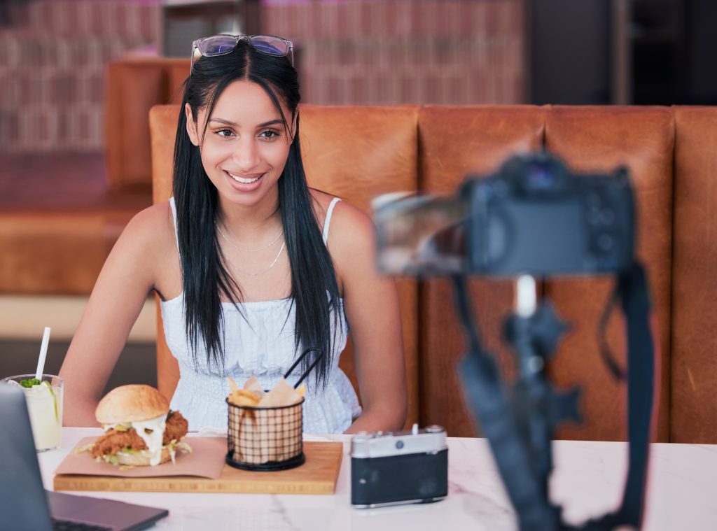 Food influencer filming a restaurant review with a burger, fries, and drink in front of her.