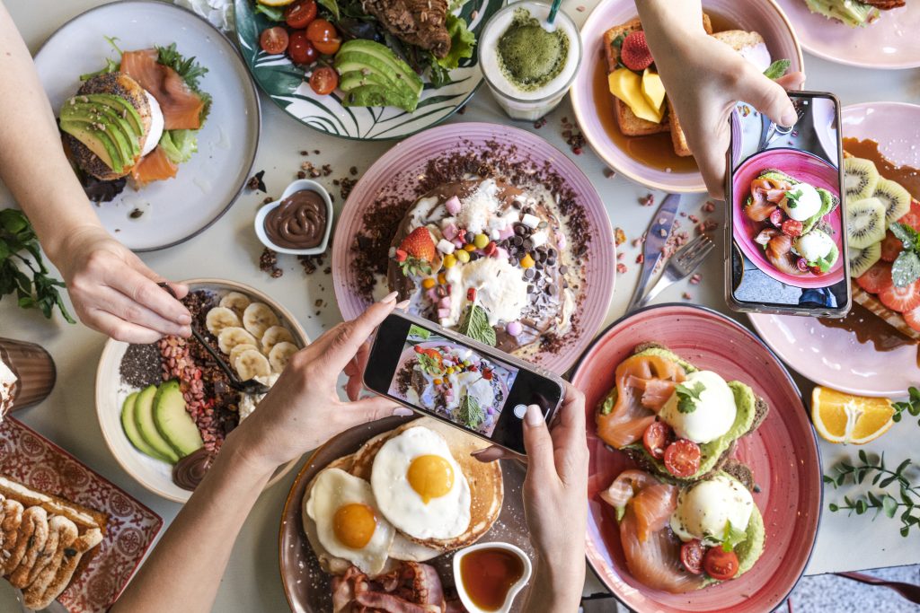 Diners taking photos of colorful brunch dishes with smartphones for Instagram and TikTok content
